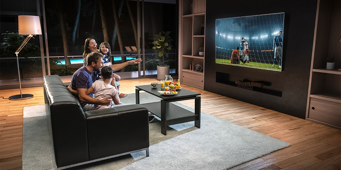 A family enjoys watching a soccer game on a large TV while sitting on a couch in a modern living room.