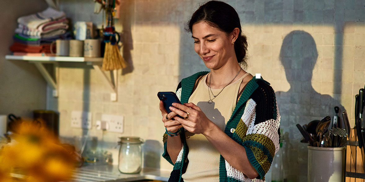 A woman smiles while looking at her smartphone.