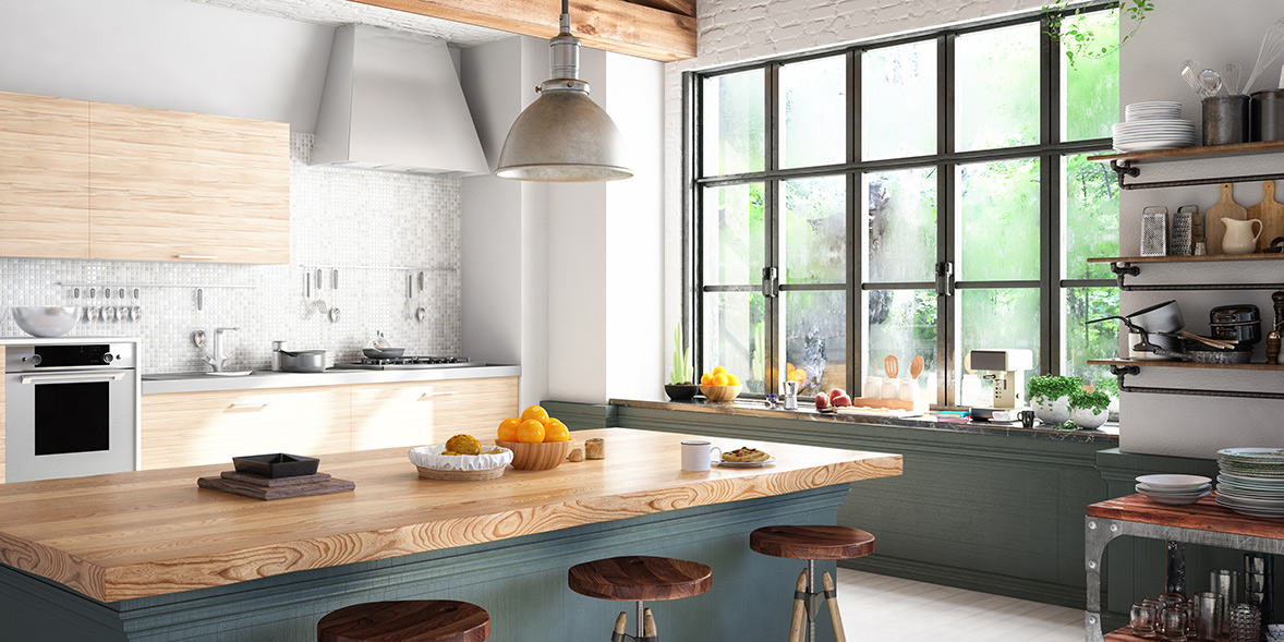Bright kitchen with wooden countertops, three stools, modern appliances, and large windows showcasing greenery outside.