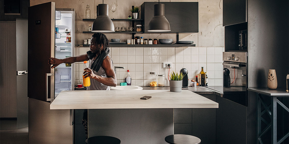 Person reaching into a refrigerator in a modern kitchen with dark cabinetry, a white countertop, and potted plants.
