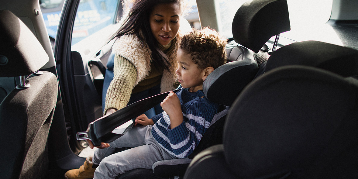 A woman helps a young boy fasten his seatbelt in a car, both focused on ensuring safety.