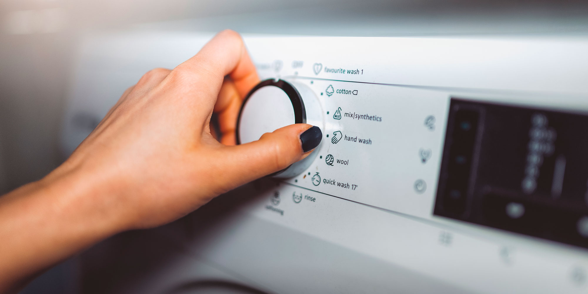 A hand adjusts a washing machine dial, selecting a wash cycle from options like cotton, hand wash, and quick wash.