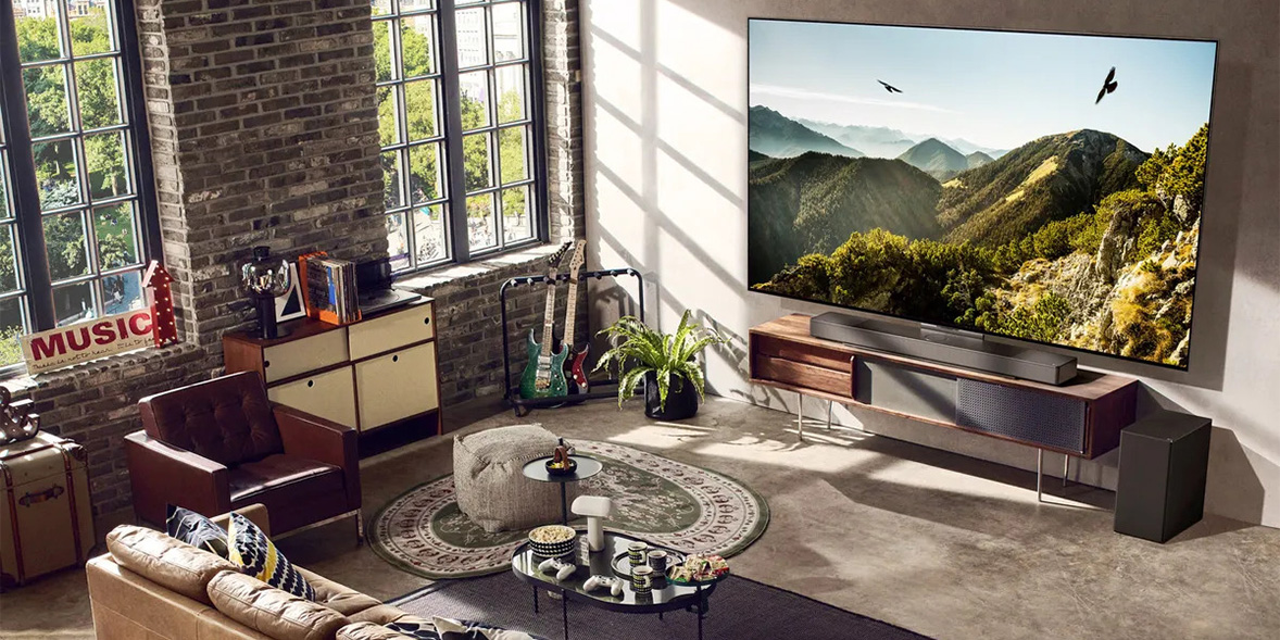 Modern living room with a large TV displaying mountains, a patterned rug, a guitar, and a cozy brown armchair by a window.