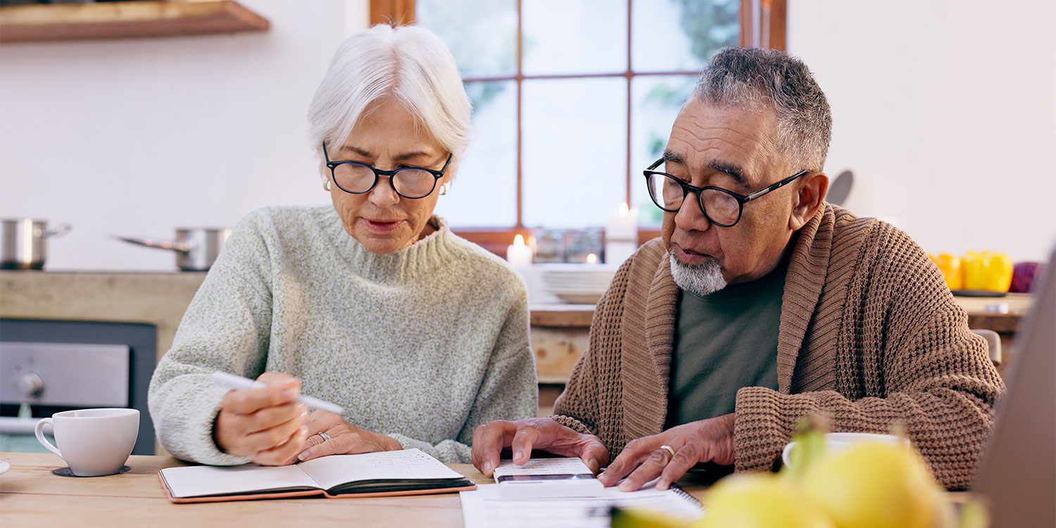Elderly couple at a kitchen table, reviewing notes and documents, with a cup of tea and fresh lemons in the foreground.