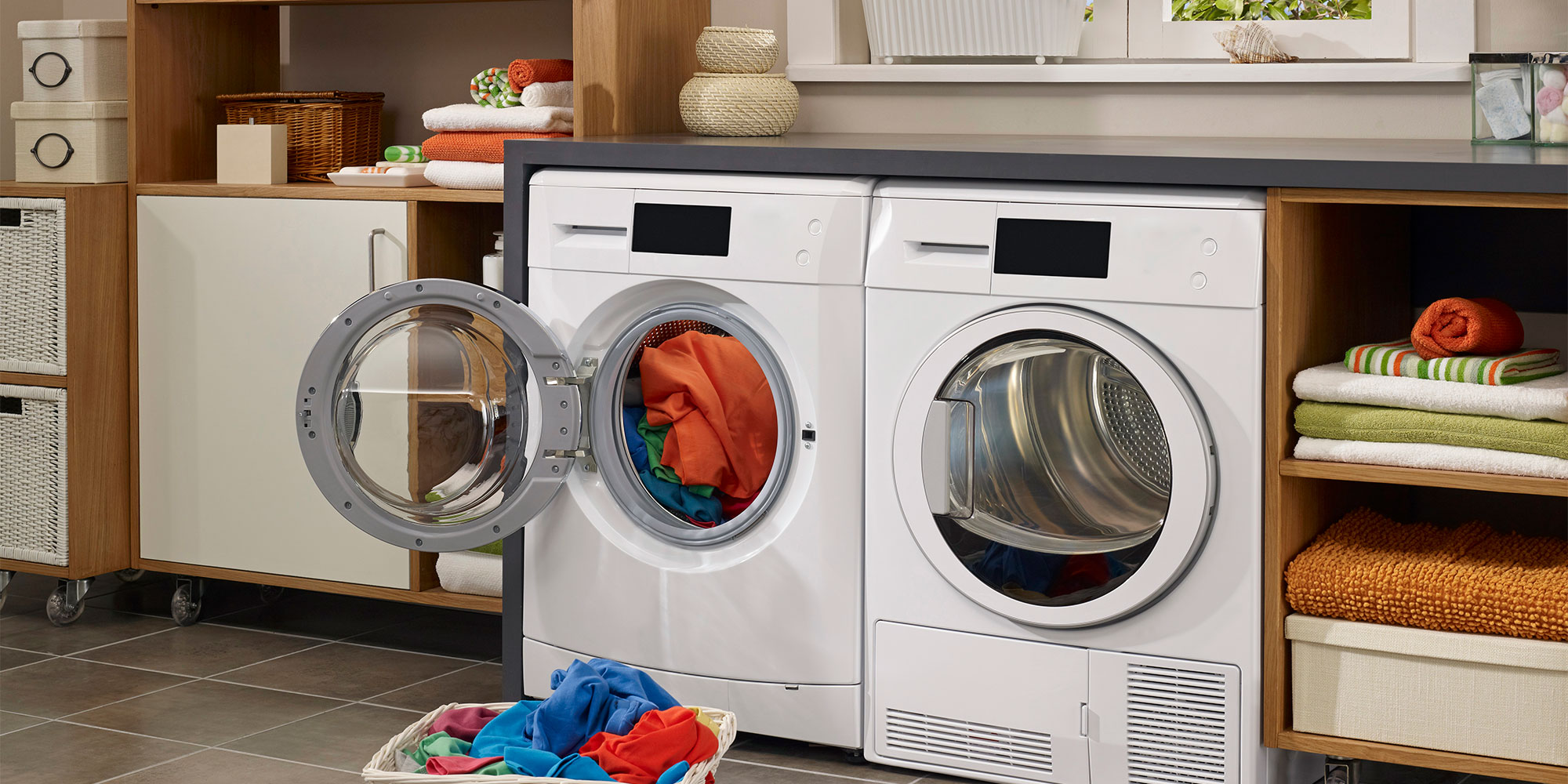 Bright laundry room with a washing machine, woven baskets, storage drawers, and colorful laundry basket on a tiled floor.