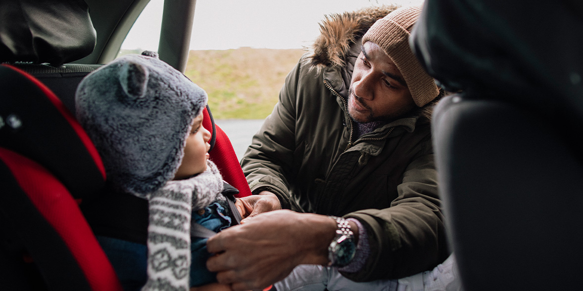 A parent secures a young child in a car seat