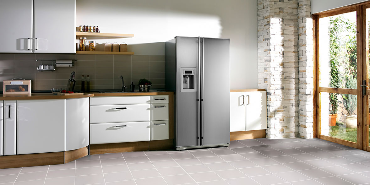 Modern kitchen featuring a sleek stainless steel refrigerator, white cabinets, wooden shelves, and a stone wall.