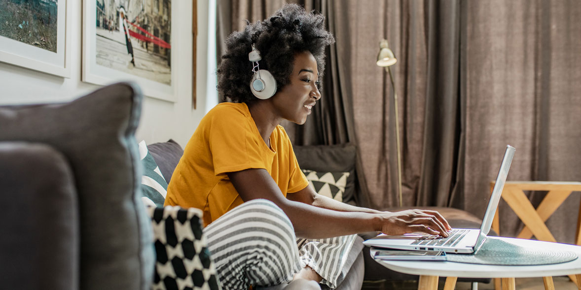 A woman sits at her laptop with headphones on