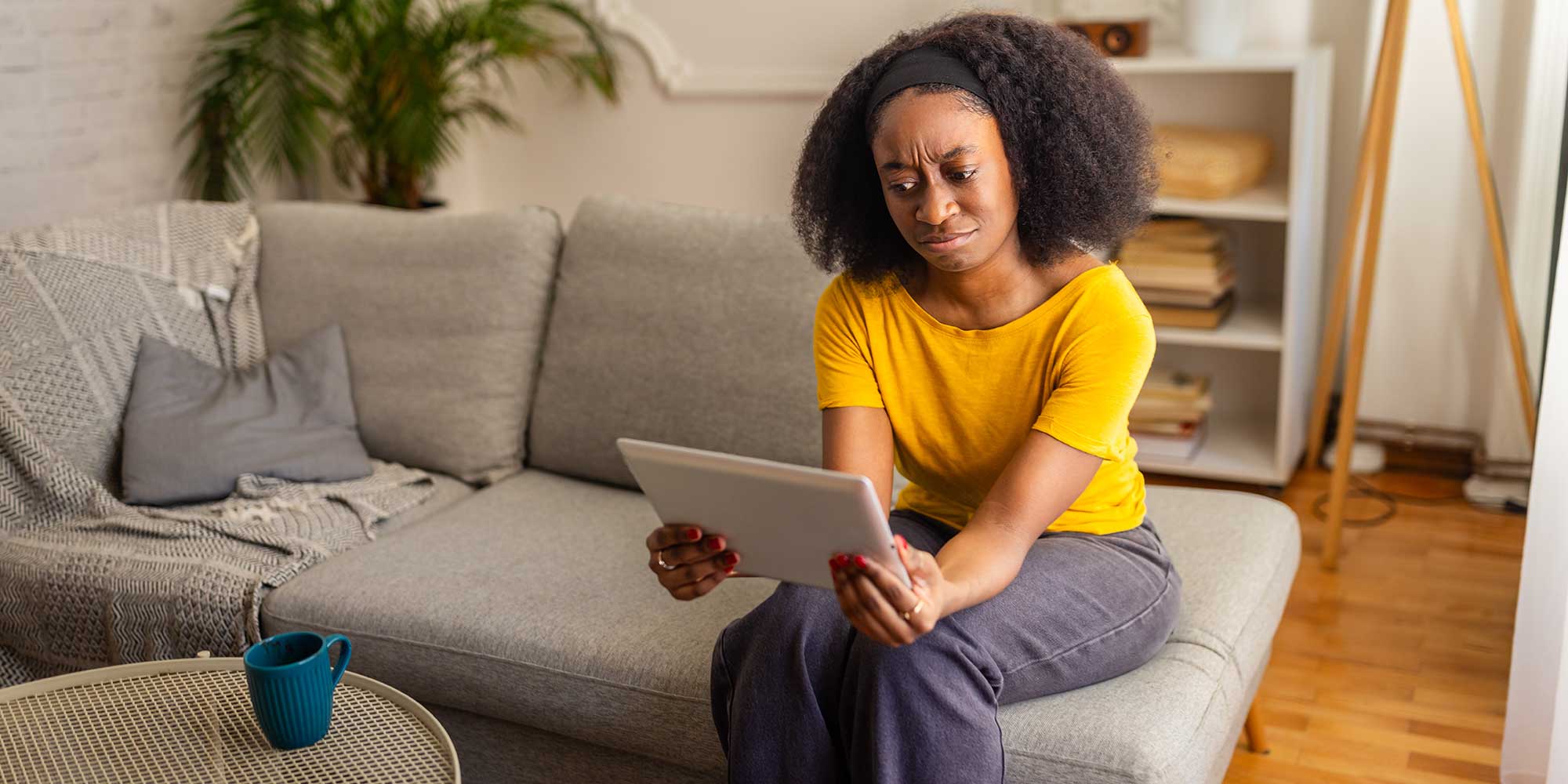 Woman looking at her energy bill in confusion, holding a tablet and sitting in a living room