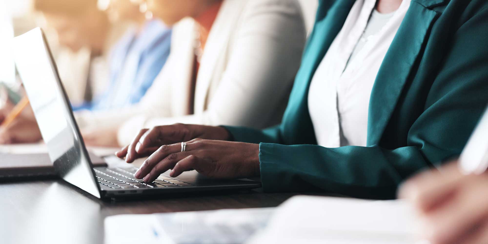 A hand rests on a white keyboard of a tablet displaying the Windows 10 interface, with a blue background and tiled menu.