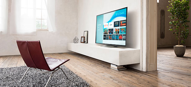 Modern living room with a large TV on a sleek white shelf, a red chair, and a textured grey rug on wooden flooring.