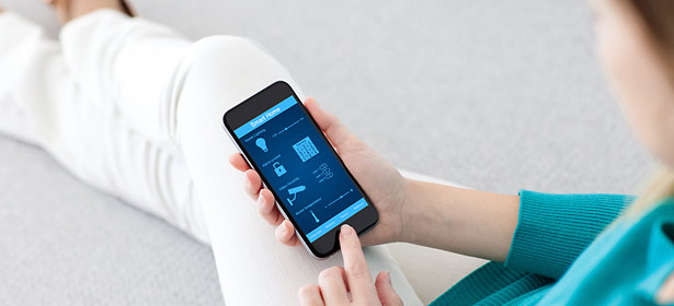 A person in a turquoise sweater sits on the floor, holding a smartphone displaying various app icons and options.