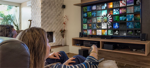 A person sits on a couch, gazing at a television displaying a vibrant grid of colorful images and designs.
